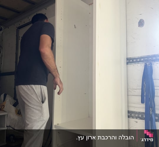 אדם מרכיב ארון לבן בתוך משאית הובלה